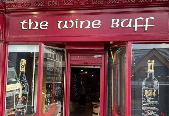 Picture of The Wine Buff shop in Rathmines Dublin. The colour of the shop is burgundy with The Wine Buff logo in gold and two wines bottles painted on the glass windows.