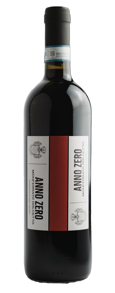 Red wine in a bordelaise shaped bottle with a black capsule and a white label with a bold red line down the middle of the label. A family crest on either side with text ANNO ZERO, DOLCETTO